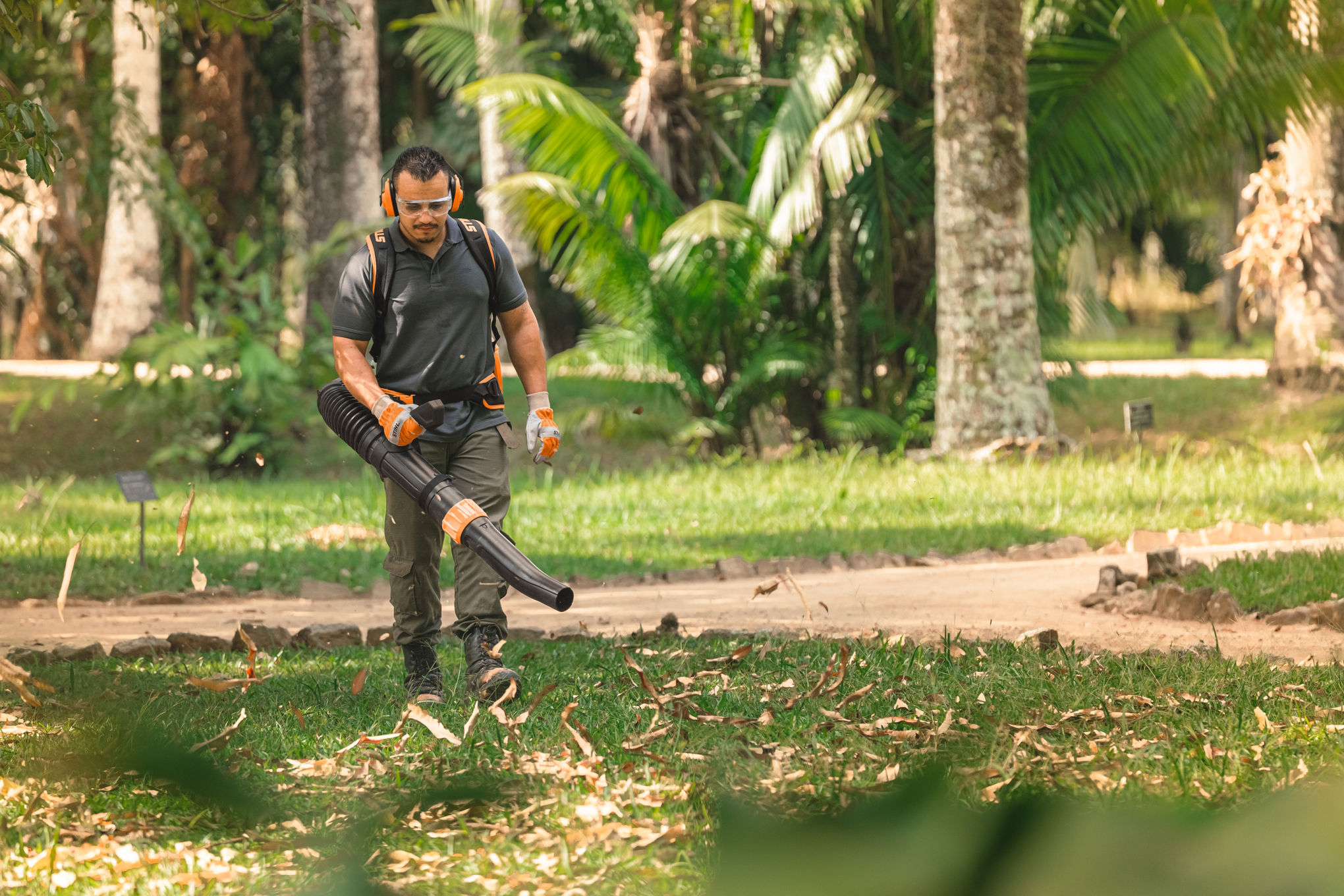 Luiz Carlos, ein Landschaftsgärtner im Botanischen Garten, bläst die Blätter mit einem Laubbläser auf dem Rasen zusammen