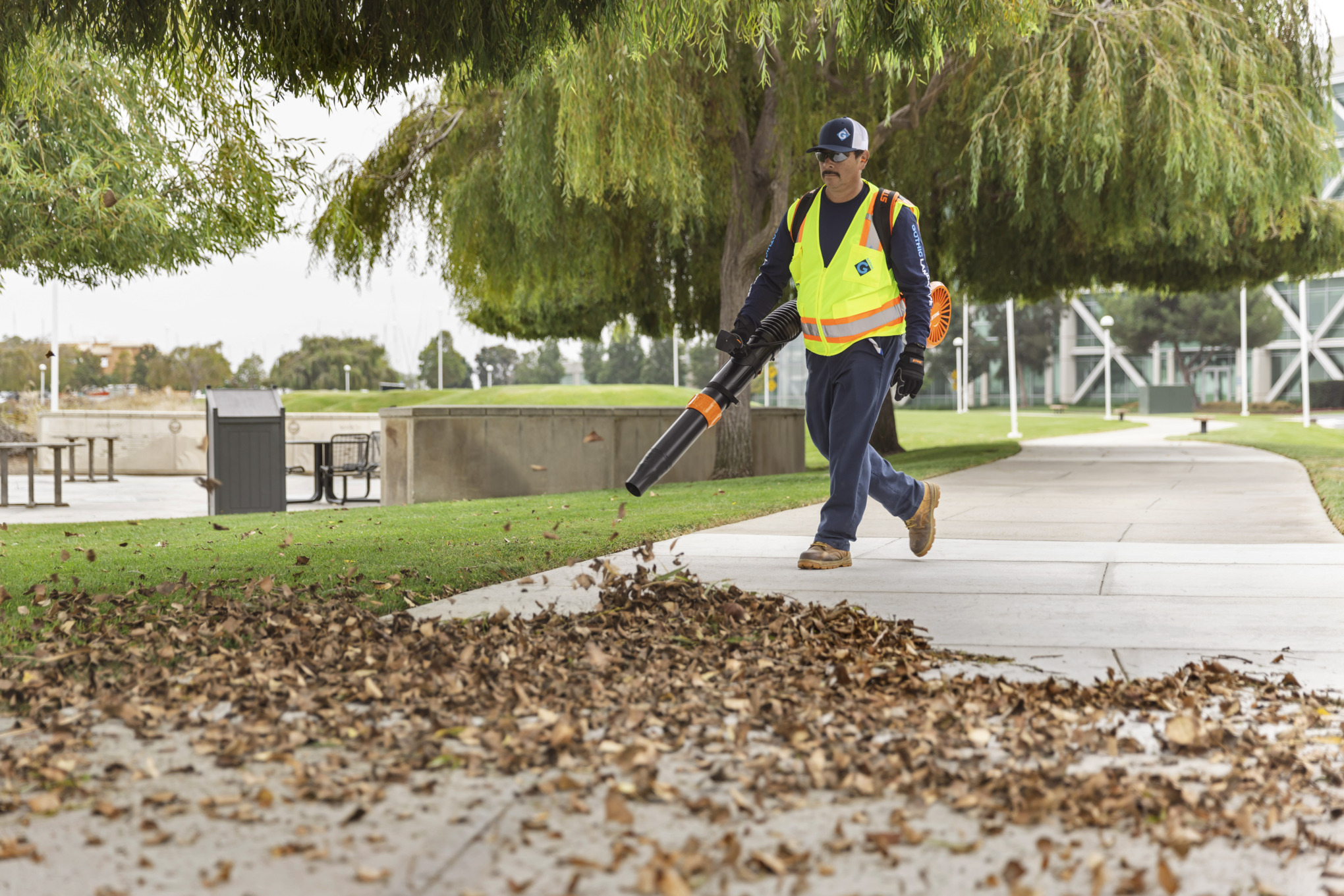 Ein Mann mit Arbeitshandschuhen bläst mit einem STIHL Laubbläser Laub vom Gehweg