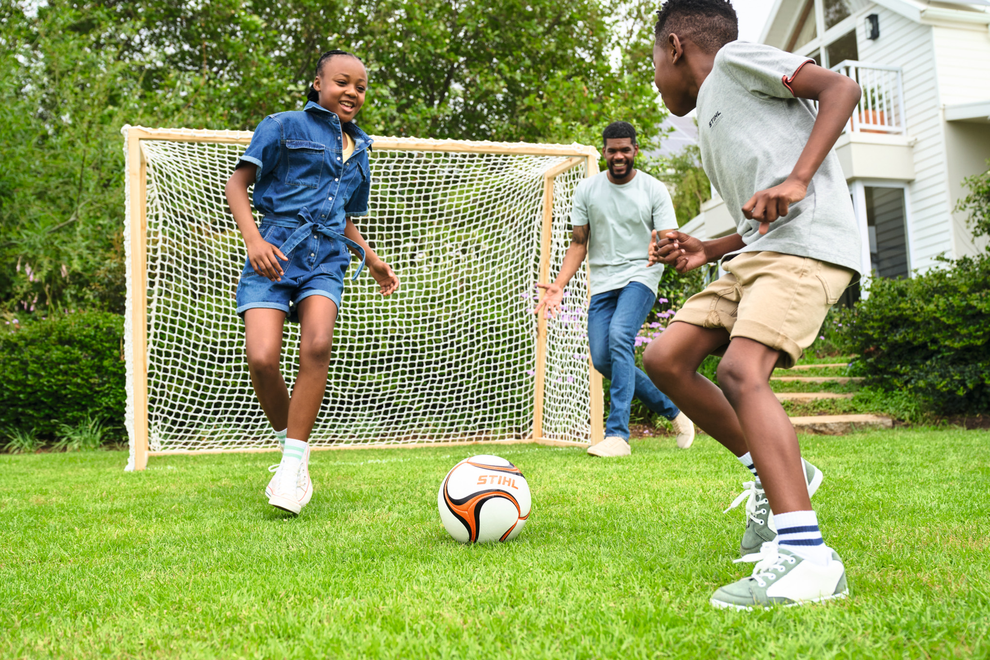 Drei Kinder spielen im Garten Fußball mit einem Fußballtor aus Holz