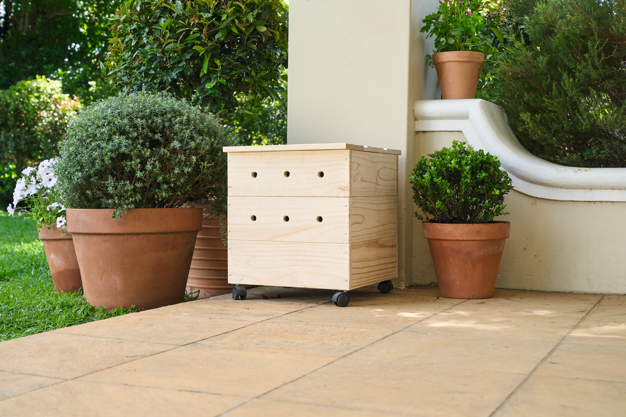 Eine geflieste Terrasse mit einer selbstgebauten Wurmkiste aus Holz, umgeben von Topfpflanzen