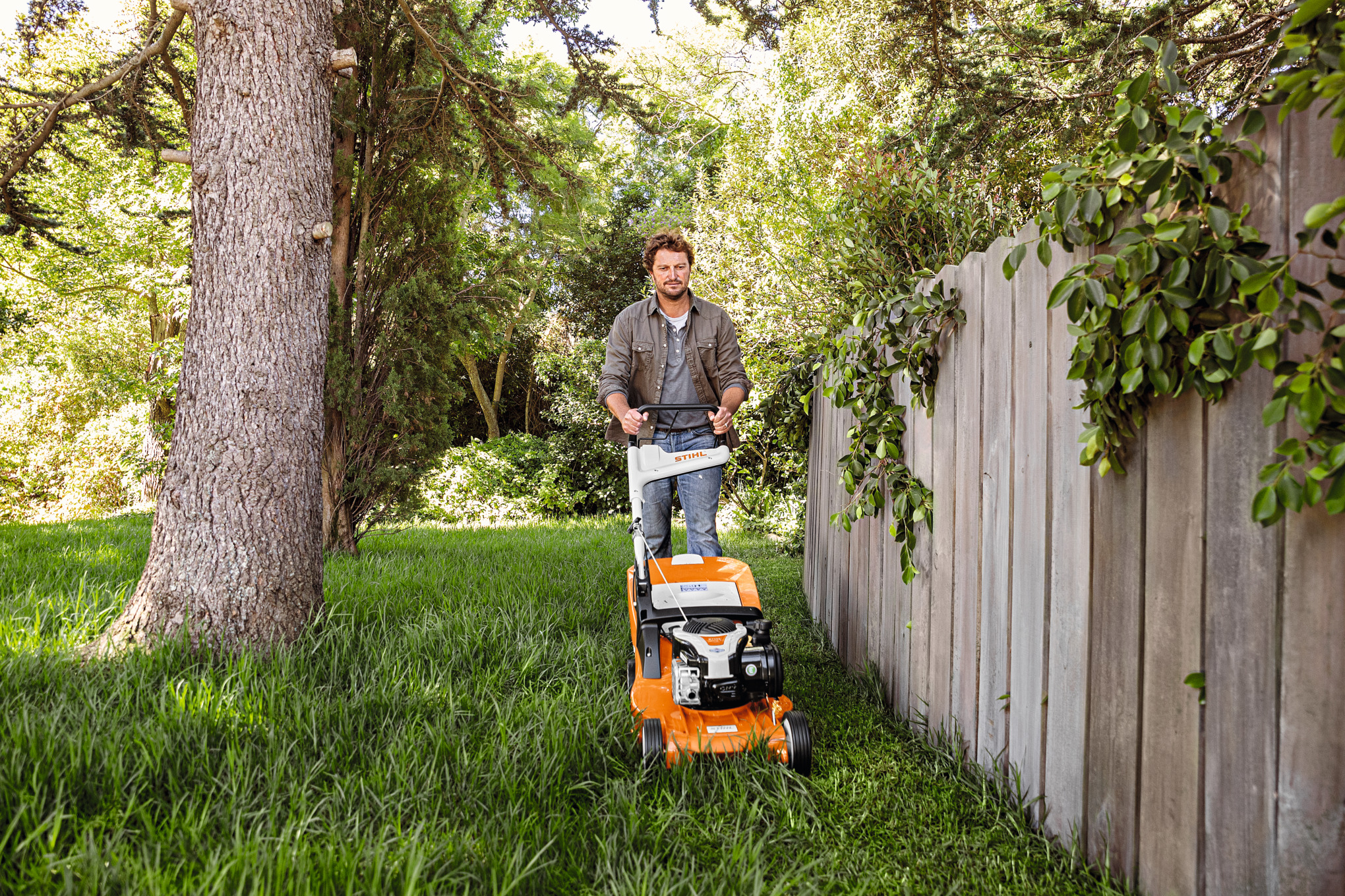 Mann betreibt mit STIHL Rasenmäher RMA 448 TC auf einem bewachsenen Grundstück Rasenpflege im Sommer