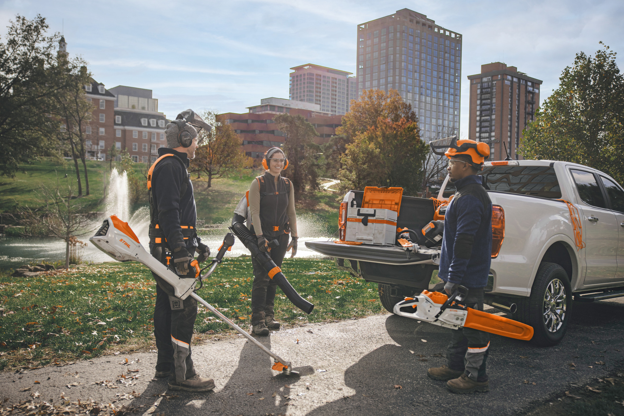 Gruppe professioneller Landschaftsgärtner, die um ihre Fahrzeuge herumstehen und sich mit STIHL-Akkuwerkzeugen auf ihre Arbeit vorbereiten.