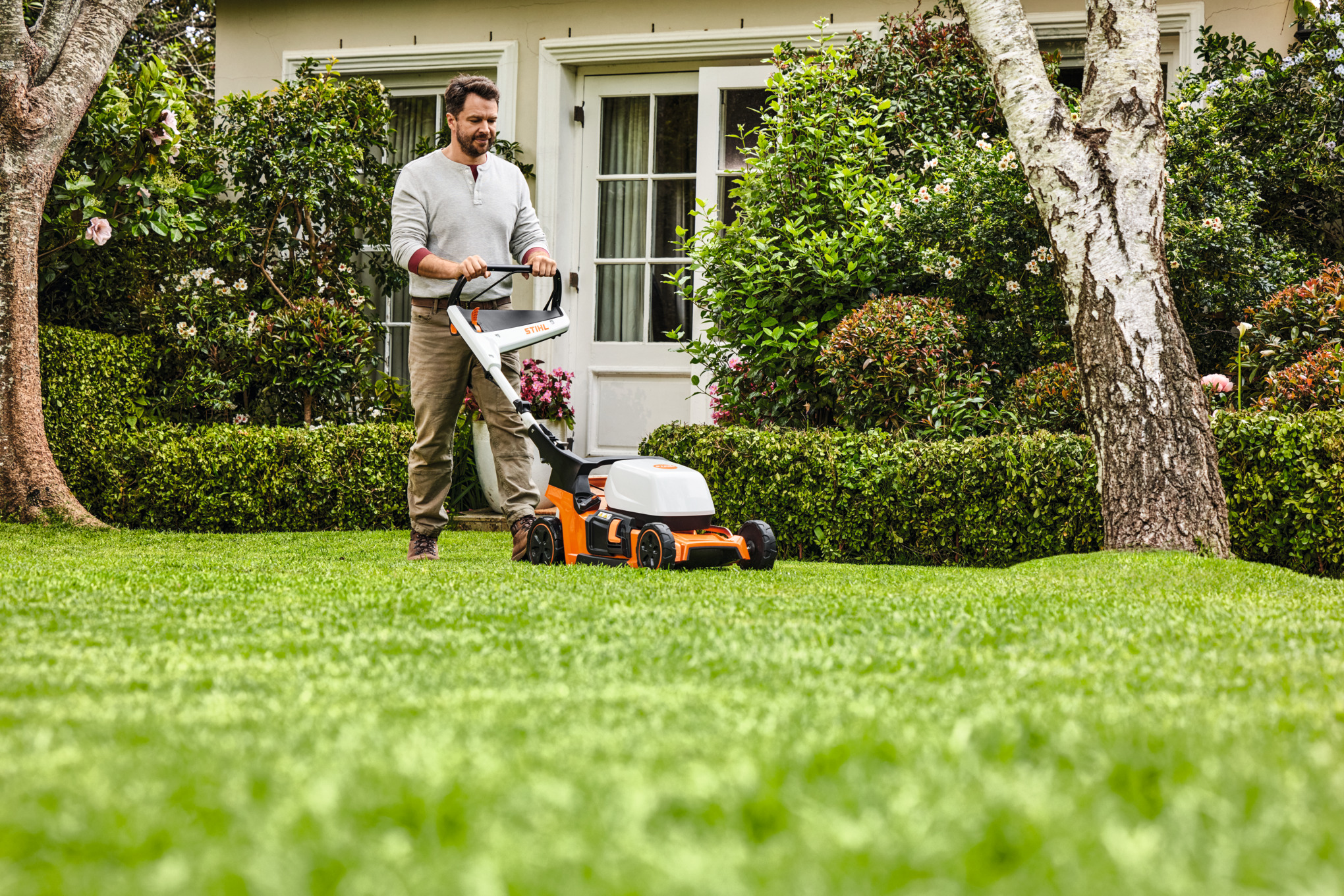Frau beim Mulchen mit einem STIHL Mulchmäher auf einem grünen Grundstück
