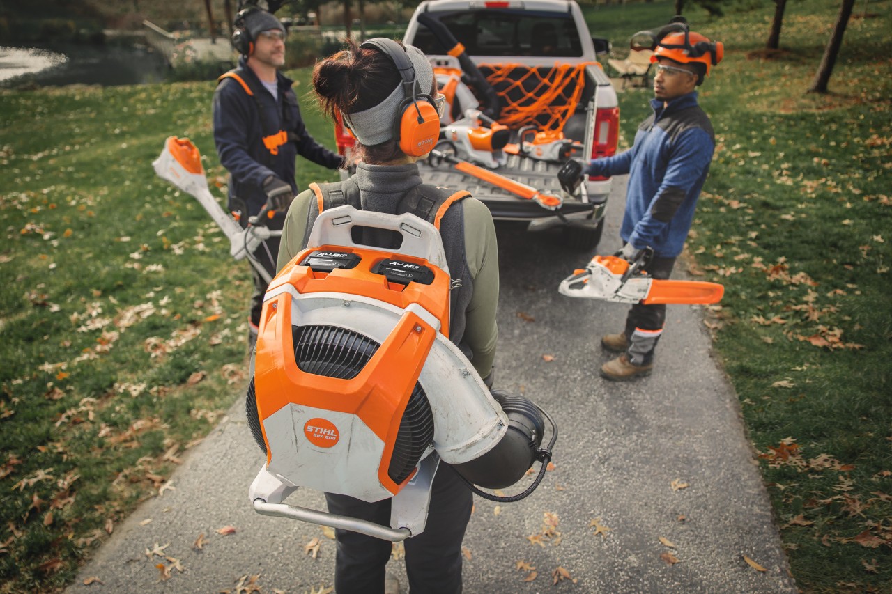Eine Gruppe professioneller Landschaftsgärtner steht um ihre Fahrzeuge herum und bereitet sich mit STIHL Akku-Geräten auf die Arbeit vor