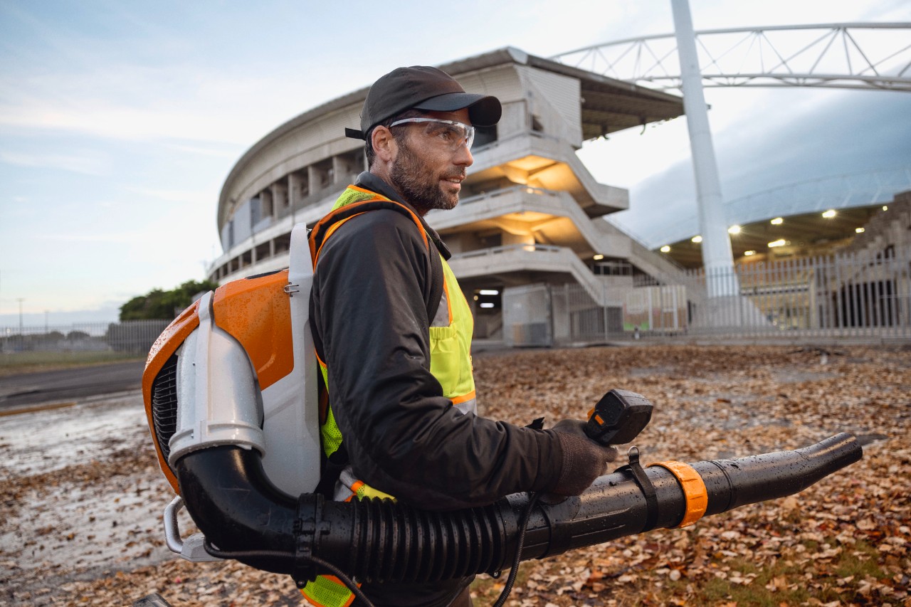 Person entfernt am späten Abend Blätter und Abfälle in einem Stadion mit dem ALLPRO Akku-Laubbläser STIHL BRA 600.